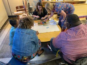 A group of Montessori educators sit around a table and work with Montessori resources with one another.